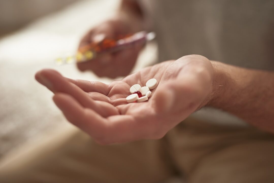 Pills In Hand Of Pensioner Man Holding Medicine.