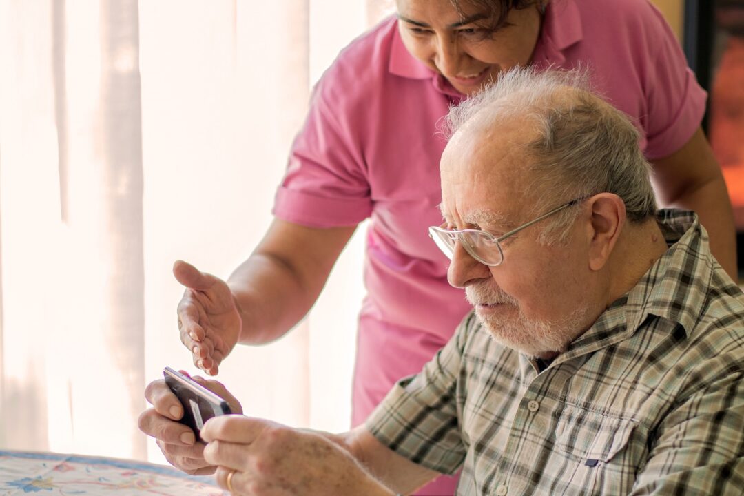 Smiling Senior Man And Caregiver With Smartphone Are Doing A Vi