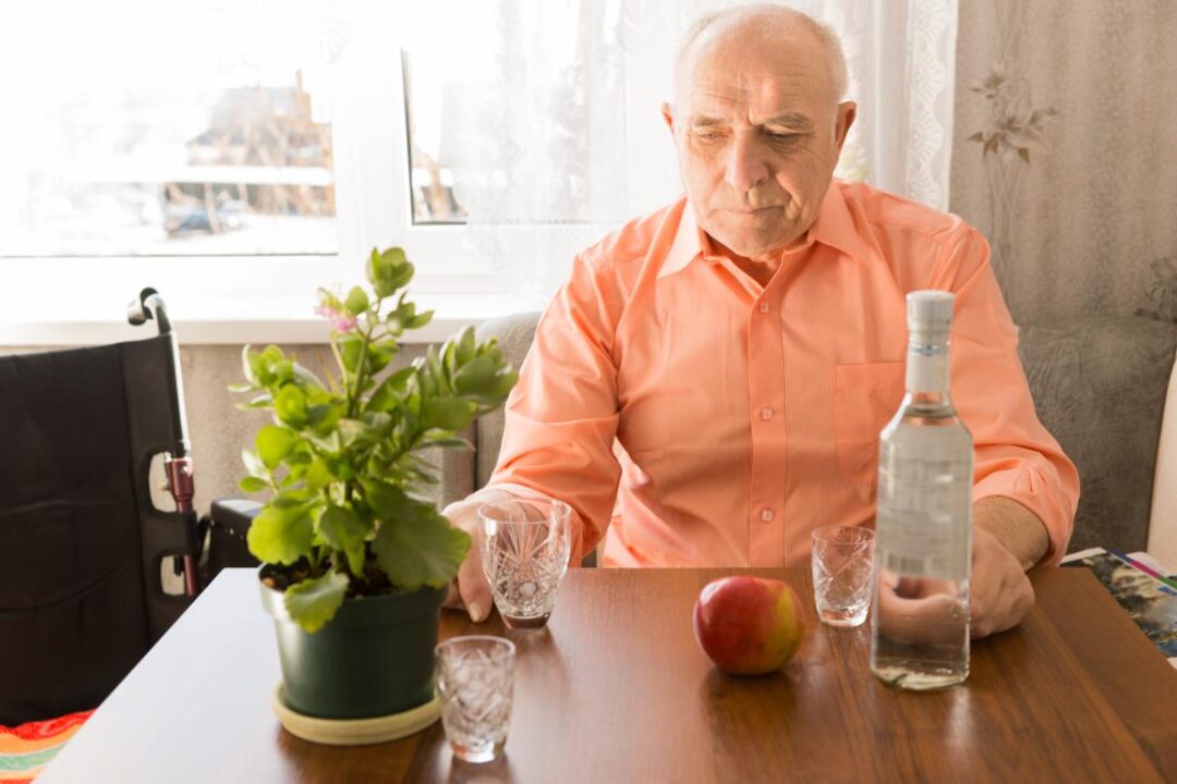 Close Up Lonely Sitting Elderly Drinking Wine At The Table With Apple And Green Plant On Top