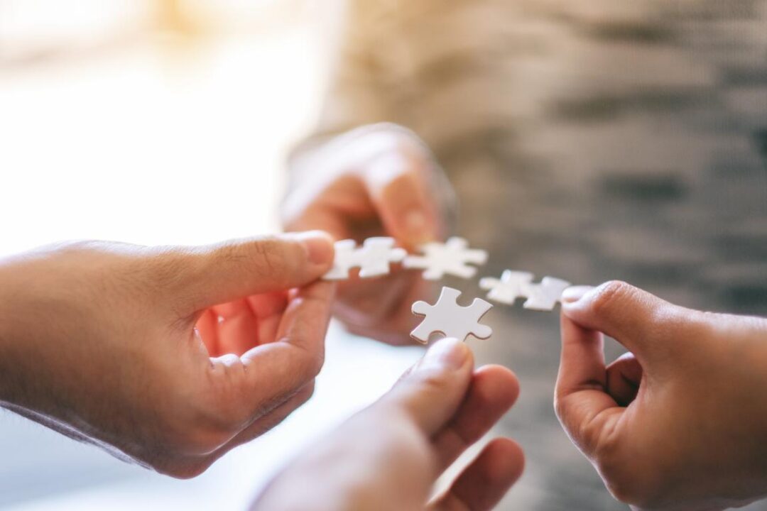 Closeup Image Of Many People Holding And Putting A Piece Of White Jigsaw Puzzle Together