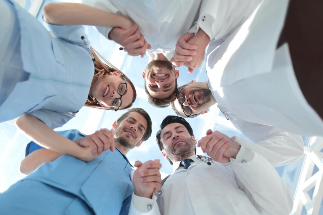 Medical Team Standing Grouped In A Circle All Looking Down At The Camera