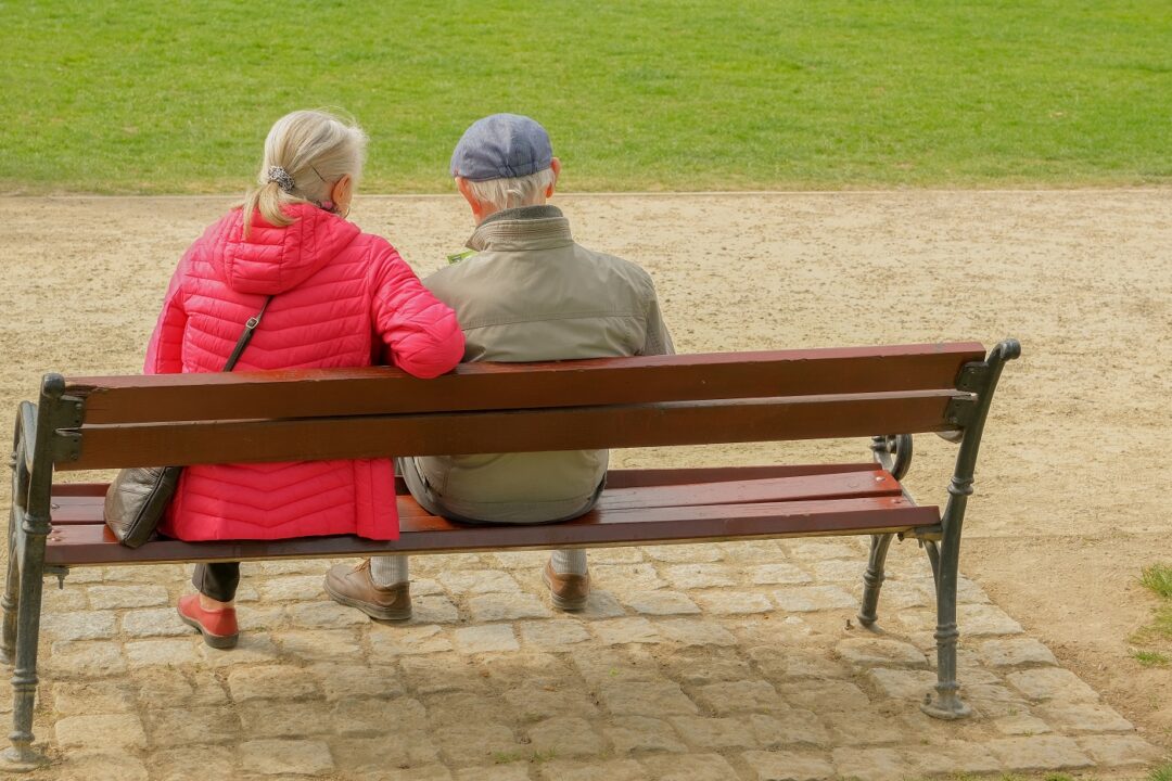 Elderly Couple Sitting On A Park Bench