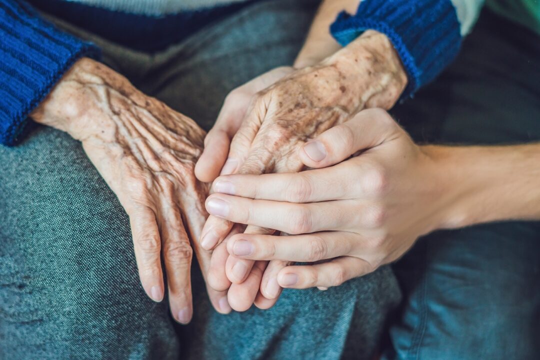 Hands Of An Old Woman And A Young Man. Caring For The Elderly. Close Up
