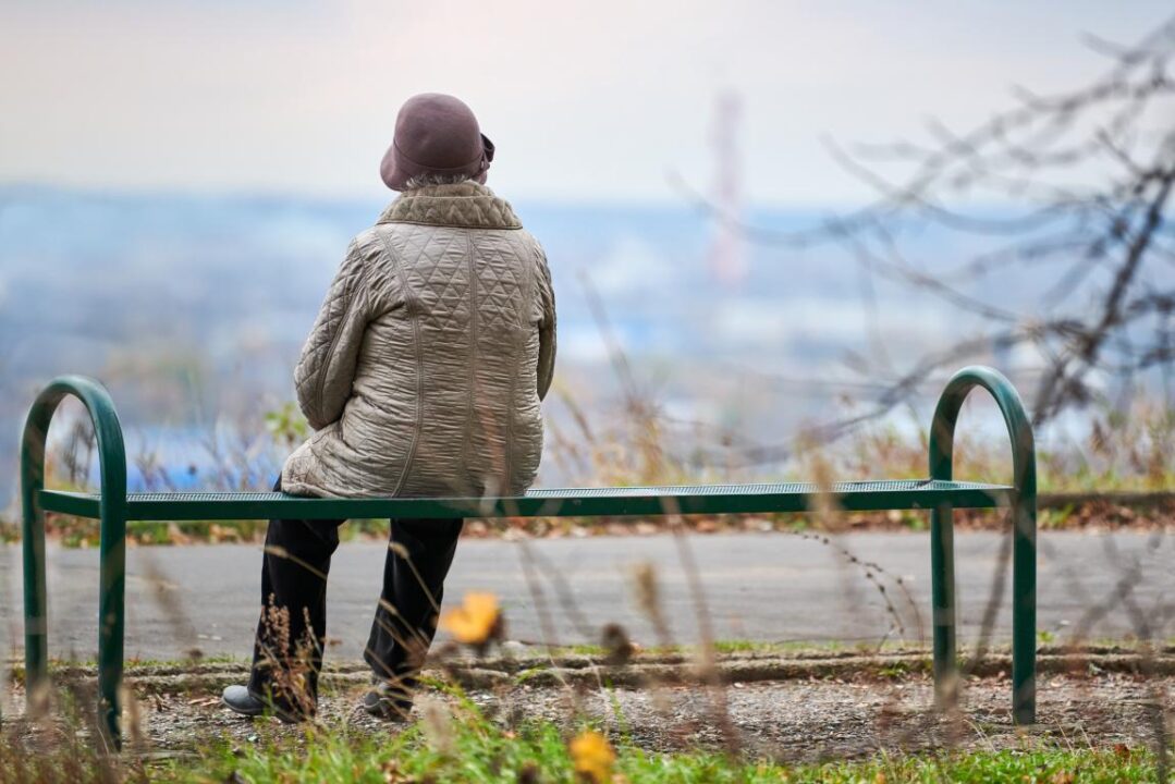 Old Woman Sitting On Bench In Autumn City Park