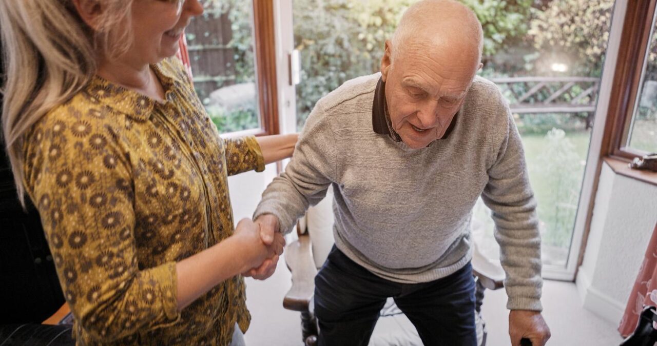 Senior Couple Help With Walking Care Support Assistance Sofa Living Room Home Elderly Woman Man With Disability Cane Lounge Retirement With Love Trust Recovery