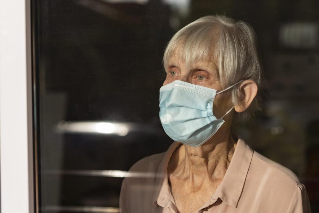 Senior Woman With Medical Mask Looking Through The Window 1