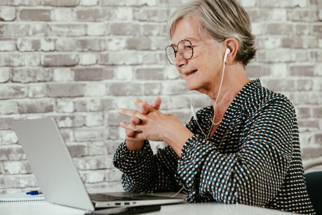 Smiling Confident Old Senior Business Woman In Video Conference With Laptop Wearing Earphones