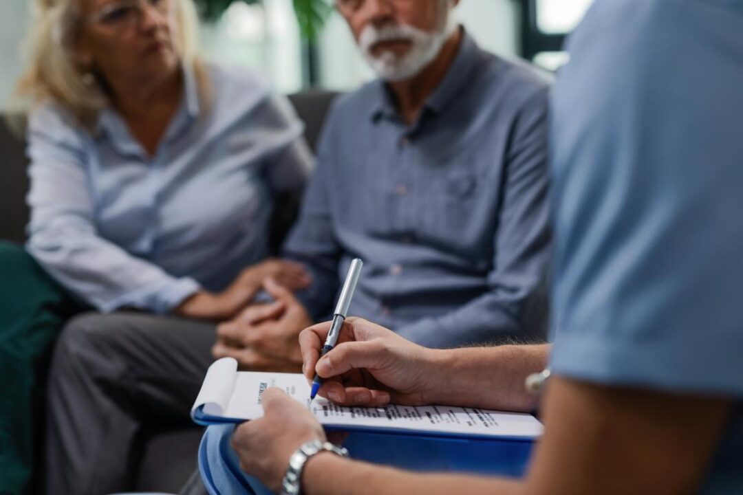 Unrecognizable Male Doctor Writing Medical Report While Visiting Senior Couple Their Home
